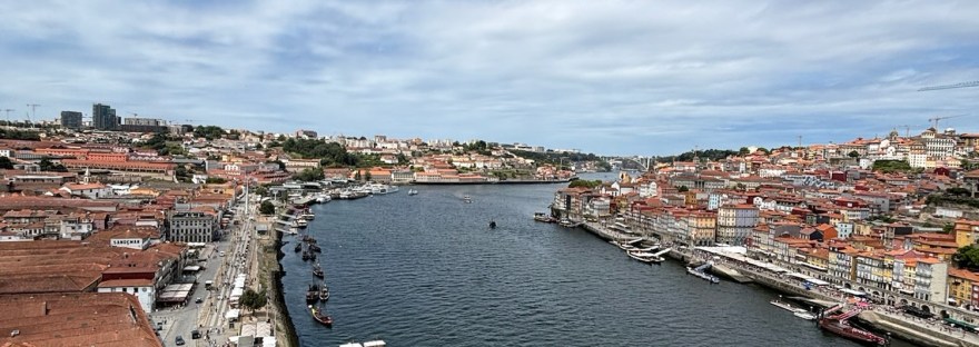 Aerial view over the Douro River in Porto, with the Ribeira district’s terracotta rooftops lining both banks and a boat cruising past.